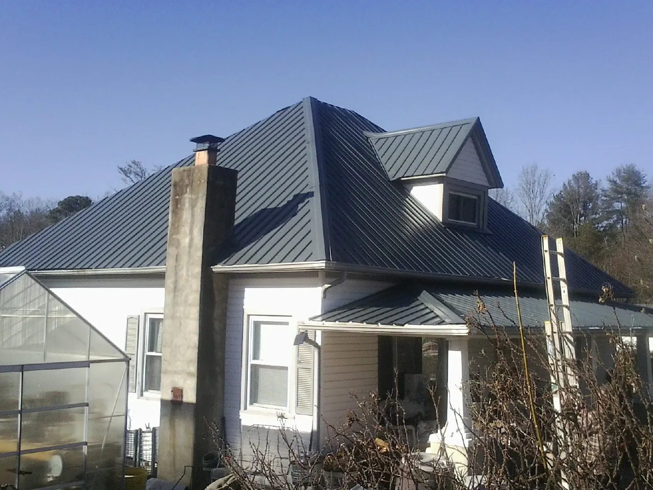 Dark blue standing seam metal roof on a white farmhouse with dormer — Slate & Tile Roof Repair by Roofing Brothers in Saint Albans