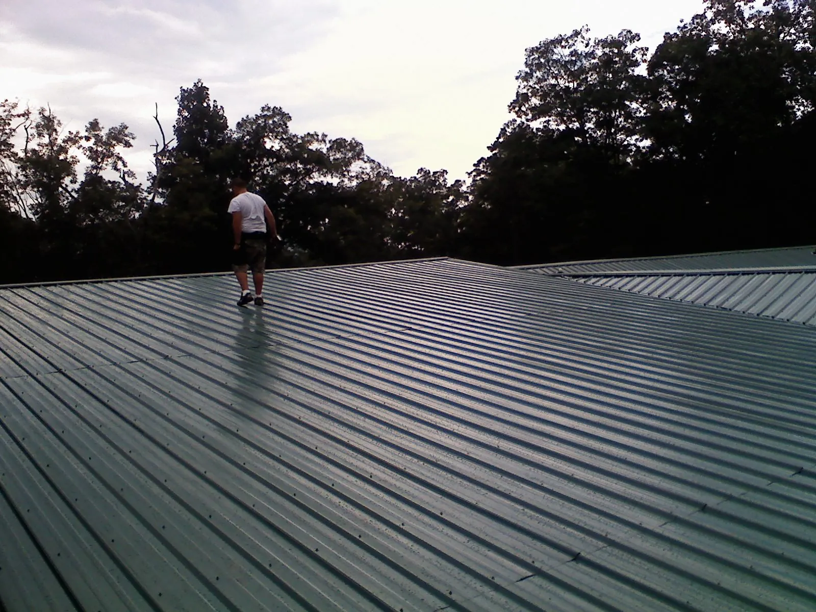 Roofer walking a wide expanse of new green metal roofing in Saint Albans
