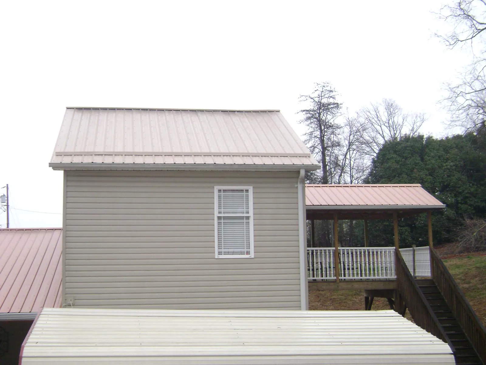Tan metal roofs on a two story addition and attached porch, from a Roof Replacement job in Saint Albans